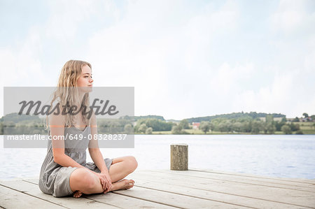 Portrait of young woman sitting on jetty, crossed legs