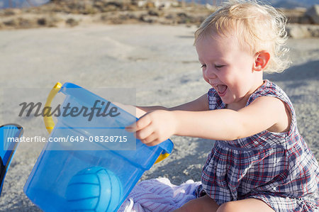 Happy female toddler playing on beach with toy bucket