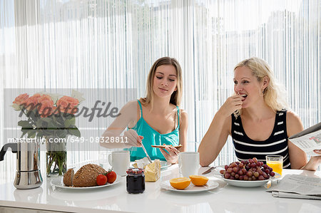 Women sitting at dining table spreading butter on bread, eating a continental breakfast together