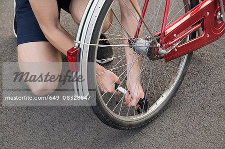 Cropped view of young man kneeling inflating bicycle tyre