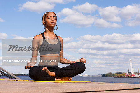 Young woman sitting cross legged by water in yoga position, eyes closed, Philadelphia, Pennsylvania, USA