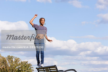 Young woman wearing crop top balancing on back on park bench