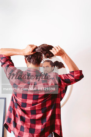 Young man looking in mirror, putting hair in ponytail, rear view
