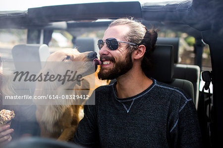 Dog licking young mans bearded face in jeep