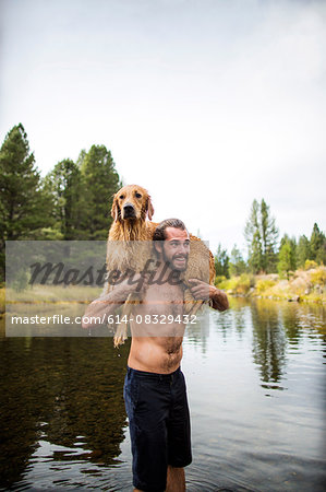 Young man carrying wet dog over shoulders in river, Lake Tahoe, Nevada, USA