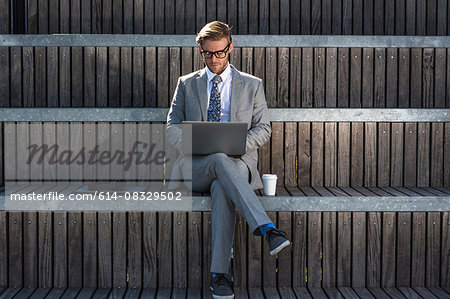 Suited young businessman typing on laptop on city stair