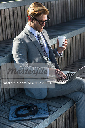 Young businessman typing on laptop on city stair