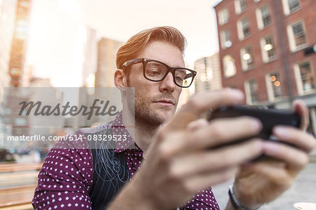 Serious young businessman reading smartphone text at sidewalk cafe, New York, USA