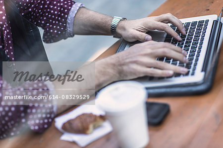 Cropped view of young businessman typing on laptop keyboard at sidewalk cafe