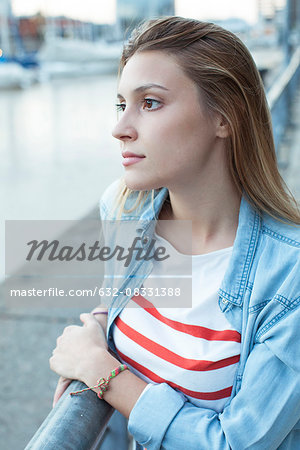 Young woman leaning against railing, looking at view of water