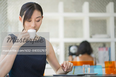 Woman drinking coffee in cafe, looking at digital tablet