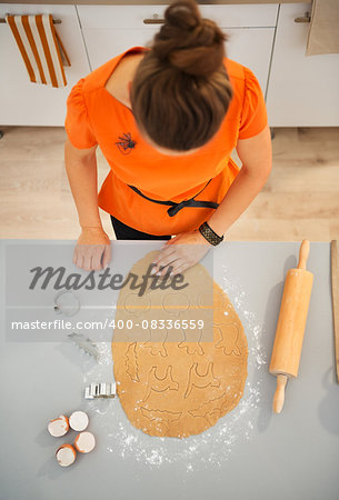 Housewife cutting out Halloween biscuits with pastry cutter from rolled pastry in kitchen. Traditional autumn holiday. Upper view