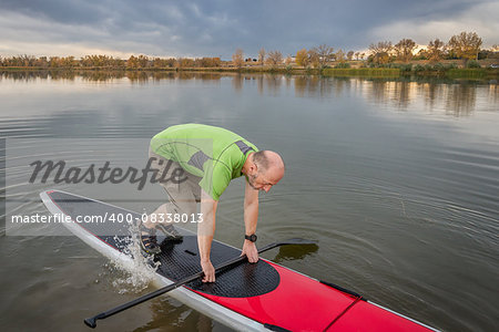 senior male is starting  paddling workout on his stand up paddleboard on a lake in Colorado