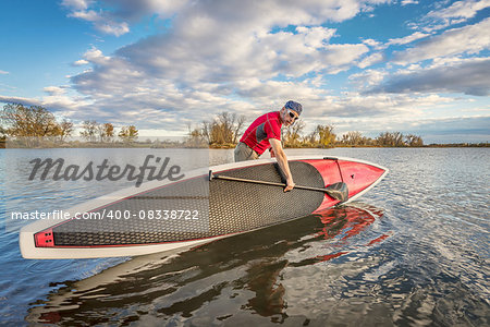 senior male launching  his 14 feet long expedition stand up paddleboard on a lake in Colorado, fall scenery