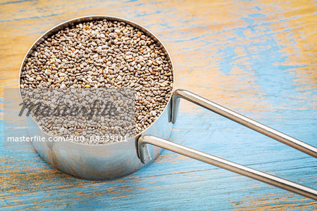 chia seeds in a metal measuring coop against white wood background