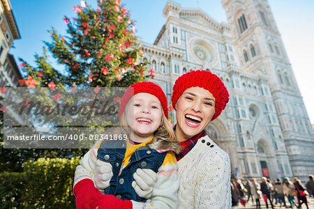 Portrait of smiling mother and daughter standing in front of Christmas tree near Duomo in Florence, Italy. Modern family enjoying carousel of Christmas time events in heart of the Renaissance.