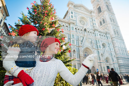Happy daughter and mother pointing on something while standing near Christmas tree and Duomo in Florence, Italy. Modern family enjoying carousel of Christmas time events in heart of the Renaissance.