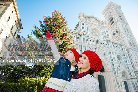 Smiling mother and daughter pointing on something while standing near Christmas tree and Duomo in Florence, Italy. Modern family enjoying carousel of Christmas time events in heart of the Renaissance.