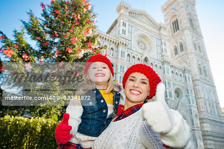 Smiling mother and daughter showing thumbs up in front of Christmas tree near Duomo in Florence, Italy. Modern family enjoying carousel of Christmas time events in heart of the Renaissance.