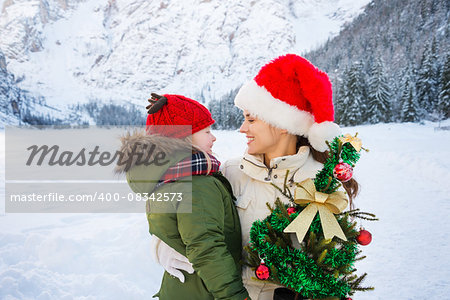 Winter outdoors on Christmas can be fairytale-maker for a children or even an adults. Happy mother and child with Christmas tree hugging in the front of snowy mountains