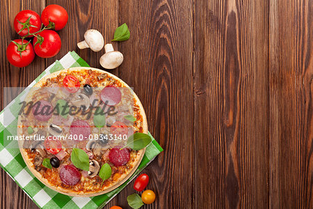 Italian pizza with pepperoni, tomatoes, olives and basil on wooden table. Top view with copy space