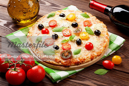 Italian pizza with cheese, tomatoes, olives, basil and red wine on wooden table