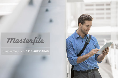 A man in shirt and tie using a handheld digital tablet in an urban scene.