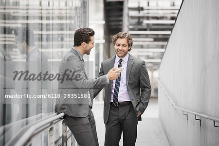 Two men in business suits outside a large building, one holding a smart phone.