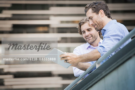 Two men on an urban walkway, looking at a digital tablet.