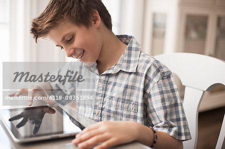 A boy seated at a table using a digital tablet, hand on the touch screen.
