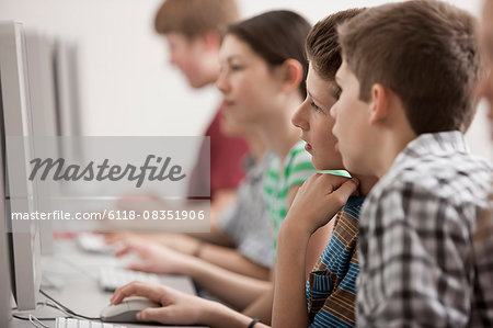 A group of young people, boys and girls, students in a computer class working at screens.