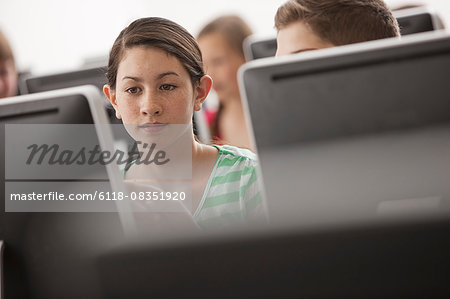 A group of young people, boys and girls, working at computer screens in class.