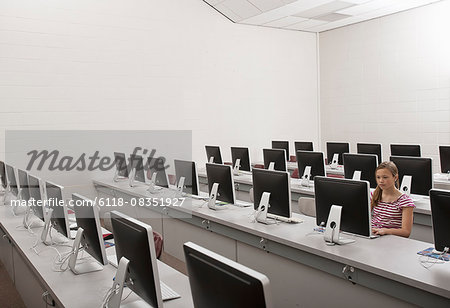 A school room, a computer lab with rows of screens and seating. A young person seated working at a terminal.