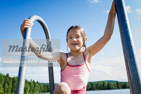 Young girl in swim suit climbing ladder out of lake, Sweden