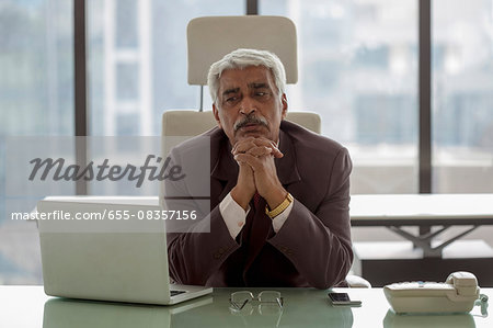 India, Portrait of senior businessman siting at desk with hands under chin