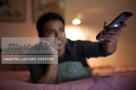 Singapore, Man lying on bed, holding remote control