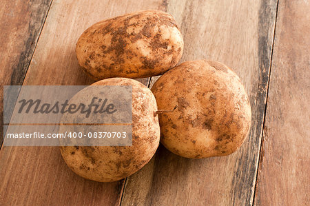 Close up Three Unwashed Fresh Potatoes on Top of a Wooden Table.
