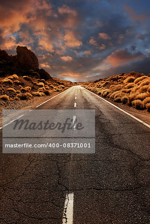 Grungy asphalt road leading through desert sunset landscape