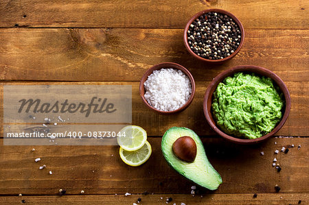 guacamole and ingredients avocado, lemon, pepper, salt on the wooden dark table top view