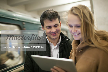 Happy young couple watching something on tablet computer in underground. Train passing by