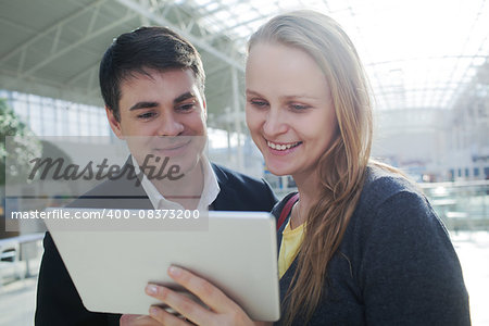 Young man and woman in shopping centre watching something on tablet PC with happy look