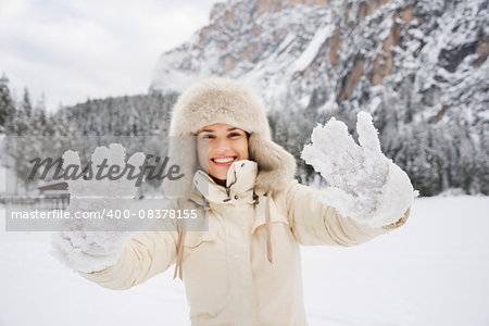 Magical mix of winter season and mountain landscape create the perfect mood. Closeup on snow-covered mittens that showing happy young woman in white coat and fur hat outdoors
