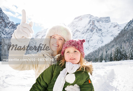 Winter outdoors can be fairytale-maker for children or even adults. Smiling mother pointing up on something to child while standing outdoors in front of snowy mountains