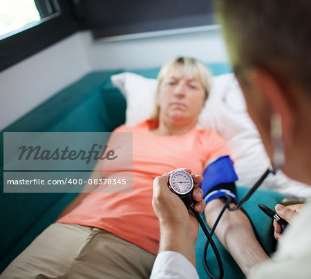 Doctor checking blood pressure of a woman patient during the visit at home. Focus on manometer