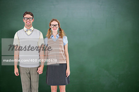 Smiling geeky hipster couple holding hands  against green chalkboard