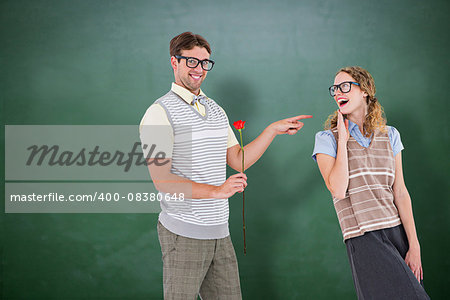 Geeky hipster holding rose and pointing his girlfriend  against green chalkboard