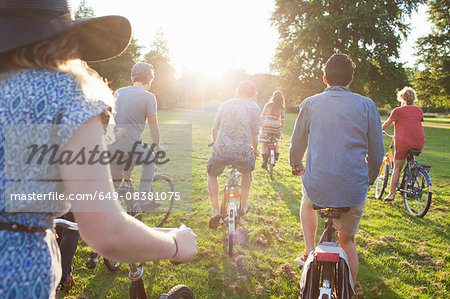 Rear view of party going adults arriving in park on bicycles at sunset