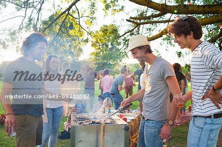 Happy adult friends barbecuing at sunset party in park