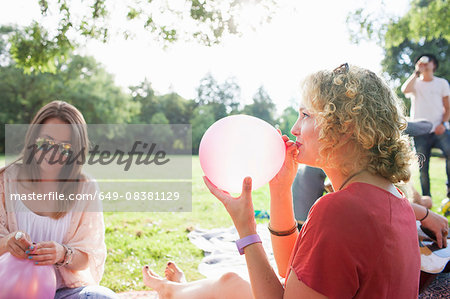 Young woman blowing up balloon at park party