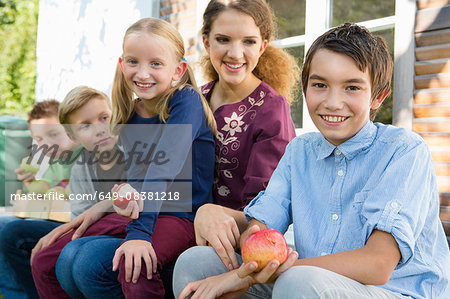 Portrait of teenagers and children sitting on patio eating apples